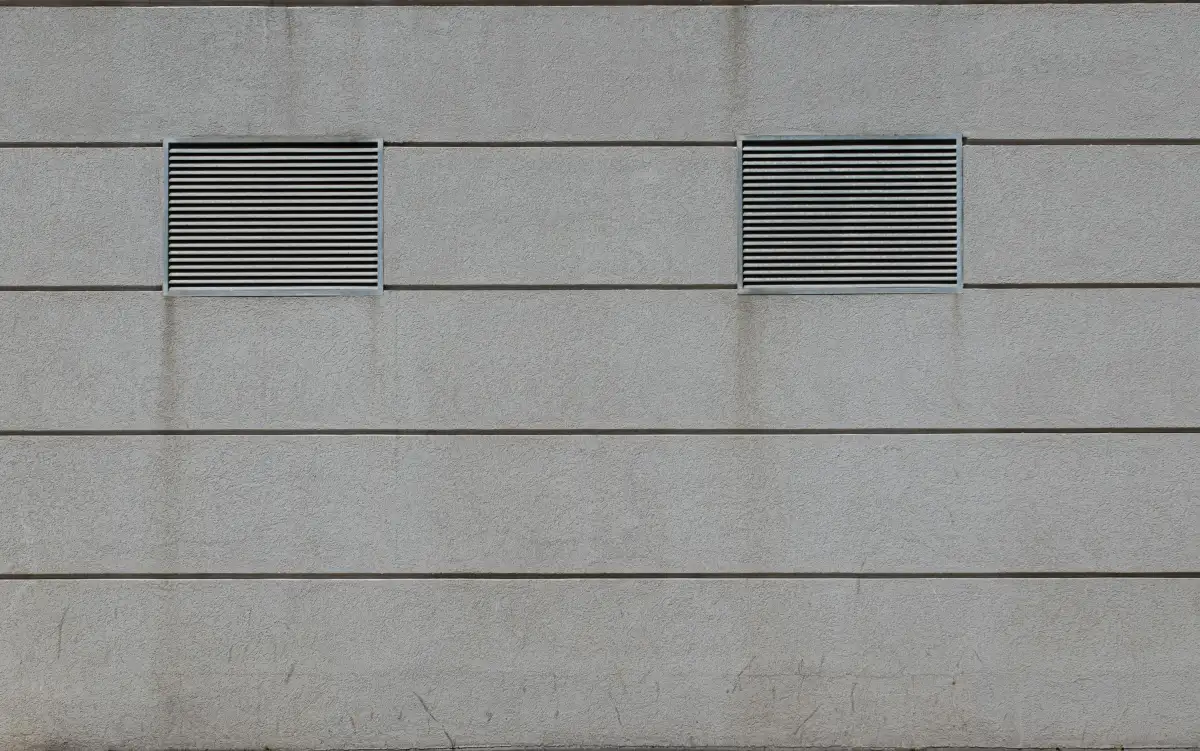 Fasad beton minimalis dengan dua ventilasi persegi sebagai lubang angin roster pada dinding bangunan
